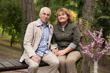 Fototapeta premium Senior elder caucasian couple together in park in spring or autumn. Wife hugging husband smile with happiness. Beautiful love relation and care of retirement old people.