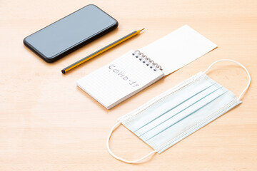 A face mask, a spiral notepad with "Covid-19" written on it, a pen and a smartphone are arranged on a wooden table. To-do list concept during the Covid-19 Outbreak.