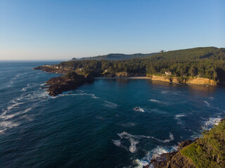 Fototapeta premium Aerial view of forest rocky coast and blue ocean waves at warm sunny day. Fantastic nature. Travel and discover concept. Wallpaper design.