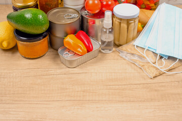 Different food and medicines donations on wooden table background with copyspace - pasta, fresh vegatables, canned food, disposable face masks, sanitizer. Food bank or delivery concept