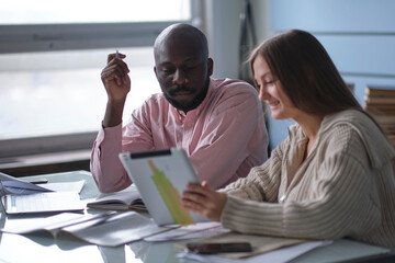 young African-American man with female colleague while working in cubicle at office. Ethnic entrepreneurs planning their work using laptop and cell phone. Staff relationship concept. selective focus