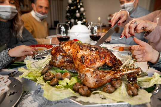 CU Of A Woman Hands With A Knife Cutting A Roast Turkey On Christmas Thanksgiving Dinner. The Members Of The Family Are Wearing Protective Face Mask. Covid Outbreak, Coronavirus Pandemic, Lockdown.