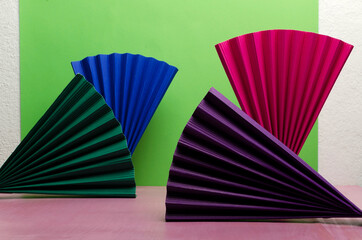 Colorful paper fan on the pink background against green wall.Empty space
