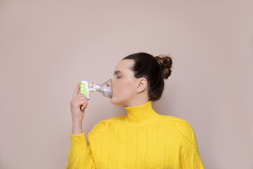 A 40-year-old woman in a yellow sweater on a pink background inhales the upper respiratory tract,...