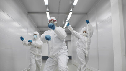 Team of medical workers in hazmat suits dancing and walking in hospital corridor