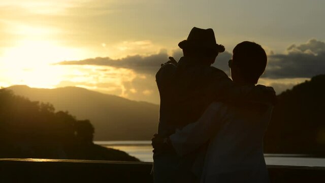 sunset on orange and yellow horizon with a silhouette of a senior couple in natural surrounding
