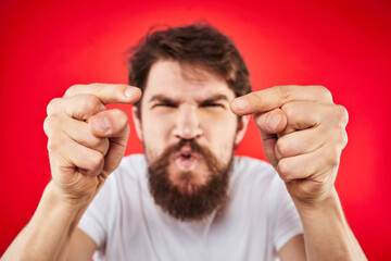 Emotional bearded man gestures with his hands in a white T-shirt aggression discontent red background