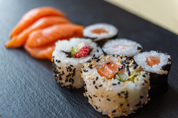 Sushi, uramaki, rolls and sashimi on a slate tray.