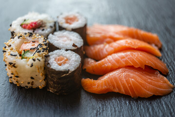 Sushi, uramaki, rolls and sashimi on a slate tray.