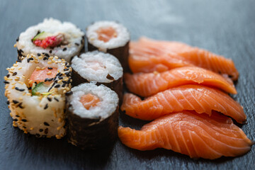 Sushi, uramaki, rolls and sashimi on a slate tray.