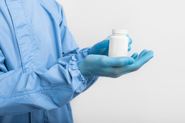 doctor in a protective medical suit, mask, glasses and gloves, holding a bottle of pills in his hands. Healthcare concept, coronavirus, COVID-19