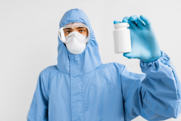 Fototapeta na wymiar doctor in a protective medical suit, mask, glasses and gloves, holding a bottle of pills in his hands. Healthcare concept, coronavirus, COVID-19
