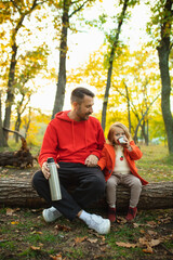 Drinking hot tea. Happy father and little cute daughter walking down the forest path in autumn sunny day. Family time, togehterness, parenting and happy childhood concept. Weekend with sincere