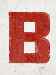 The letter B is red on a worn white background. Grunge texture of old paint in cracks and wear