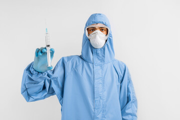 Male doctor in a protective medical suit, mask, glasses and gloves, holds a syringe with a vaccine against coronavirus, the concept of medical care