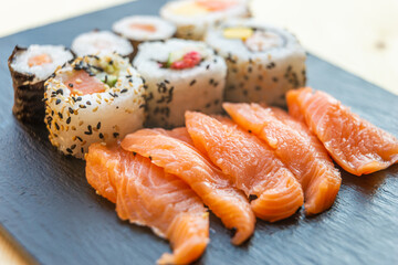 Sushi, uramaki, rolls and sashimi on a slate tray.
