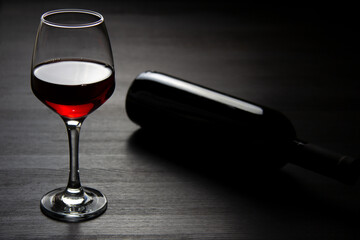 A bottle of red wine and a glass of red wine on a dark background. The concept of minimalism.