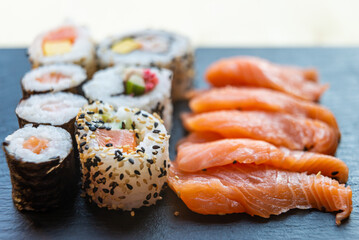 Sushi, uramaki, rolls and sashimi on a slate tray.