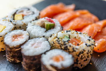 Sushi, uramaki, rolls and sashimi on a slate tray.