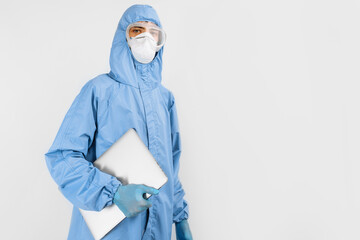 Male doctor in a protective medical suit to protect against coronavirus, in a mask, glasses and gloves, with a laptop on an isolated white background