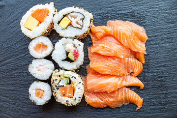 Sushi, uramaki, rolls and sashimi on a slate tray.