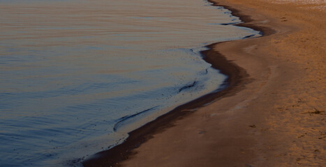 Sandy riverbank and calm river waters at sunset..