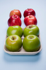 Fresh red and green apples. Green apples in a pulp paper tray. Studio photo isolated on light blue background.