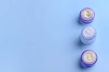 Cosmetic cream in transparent jars on color background
