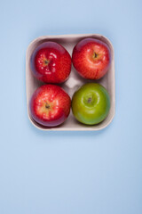 Four fresh red and green apples in a pulp paper tray. Studio photo isolated on light blue background.