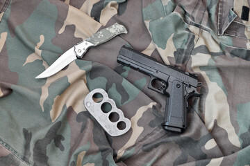 Handgun lies with brass knuckles and knife on camouflage military uniform close up. Concept of...
