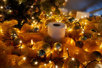 funny christmas decoration with a roll of toilet paper, golden christmas balls, small lights and orange cloth next to an artificial christmas tree