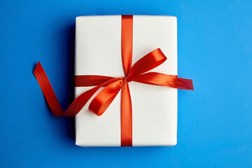 White gift box tied with red ribbon on blue background