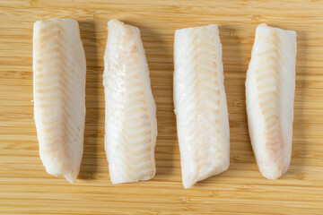 Fresh iced pieces of cod fish loins or fillets on wooden cutting board. Top view.
