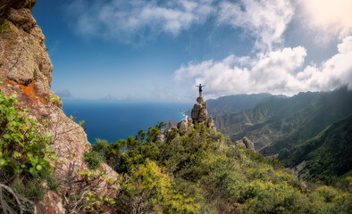 a man perched on a rock looks at the horizon with the sea and the green trees