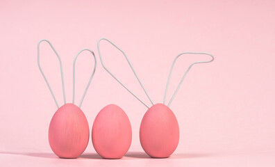 Three pink Easter eggs, cute rabbits with wire ears on a pink monochrome background with soft shadow. The concept of meeting a Happy Easter. Close-up, selective focus.