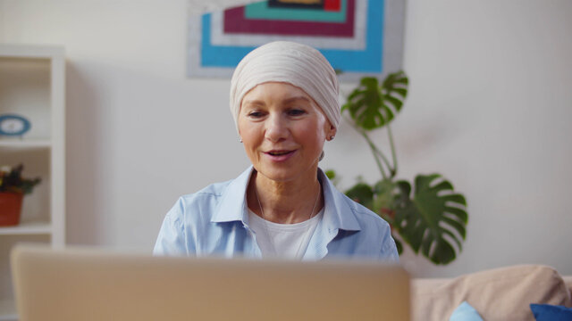 Portrait of senior woman having cancer using laptop sitting in modern home interior