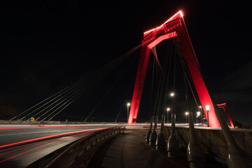 willembrug rotterdam is lit at night, with the red color contrasting nicely with the night