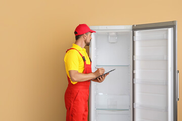 Worker of repair service near fridge on color background