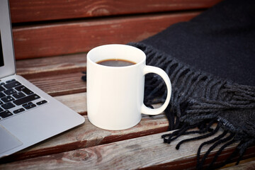 Laptop, mug with coffee on the street bench. Remote work concept during coronavirus infection. Selective focus, background blur.