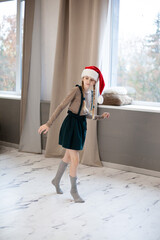 Blond girl with pigtails wearing Santa Claus hat slinking, slowly walking. Christmas and New Year is coming concept.