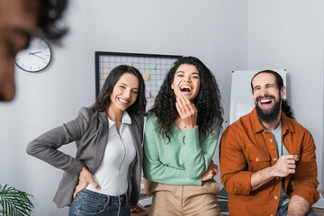 laughing hispanic businesspeople looking at colleague on blurred foreground