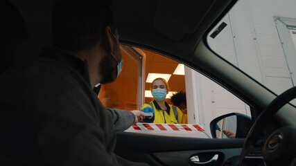 Man driver in mask showing pass card to worker in booth before entrance in pass control area