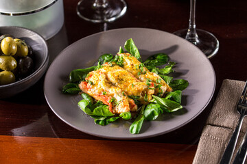 Baked salmon with cheese crust and fresh spinach on wooden table at restaurant