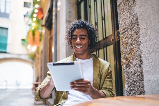 Happy young black man reading notes on tablet in cafe