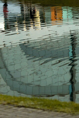 Abstract reflection in the water. Sunny day. Distorted view with ripples. Urban shot. Building windows in reflection.