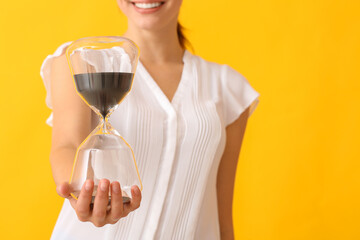 Young woman with hourglass on color background, closeup