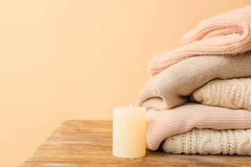 Obraz na płótnie Canvas Stylish warm clothes with candle on table against color background