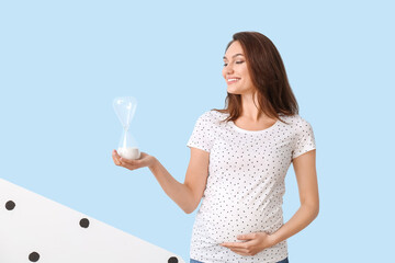 Young pregnant woman with hourglass on color background