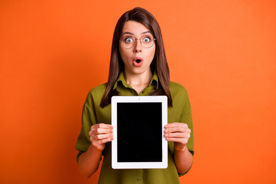 Photo portrait of amazed female student keeping tablet showing touchscreen copyspace isolated on vibrant orange color background