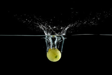 close up view of fresh lemon citrus fruit falling into water isolated on black background